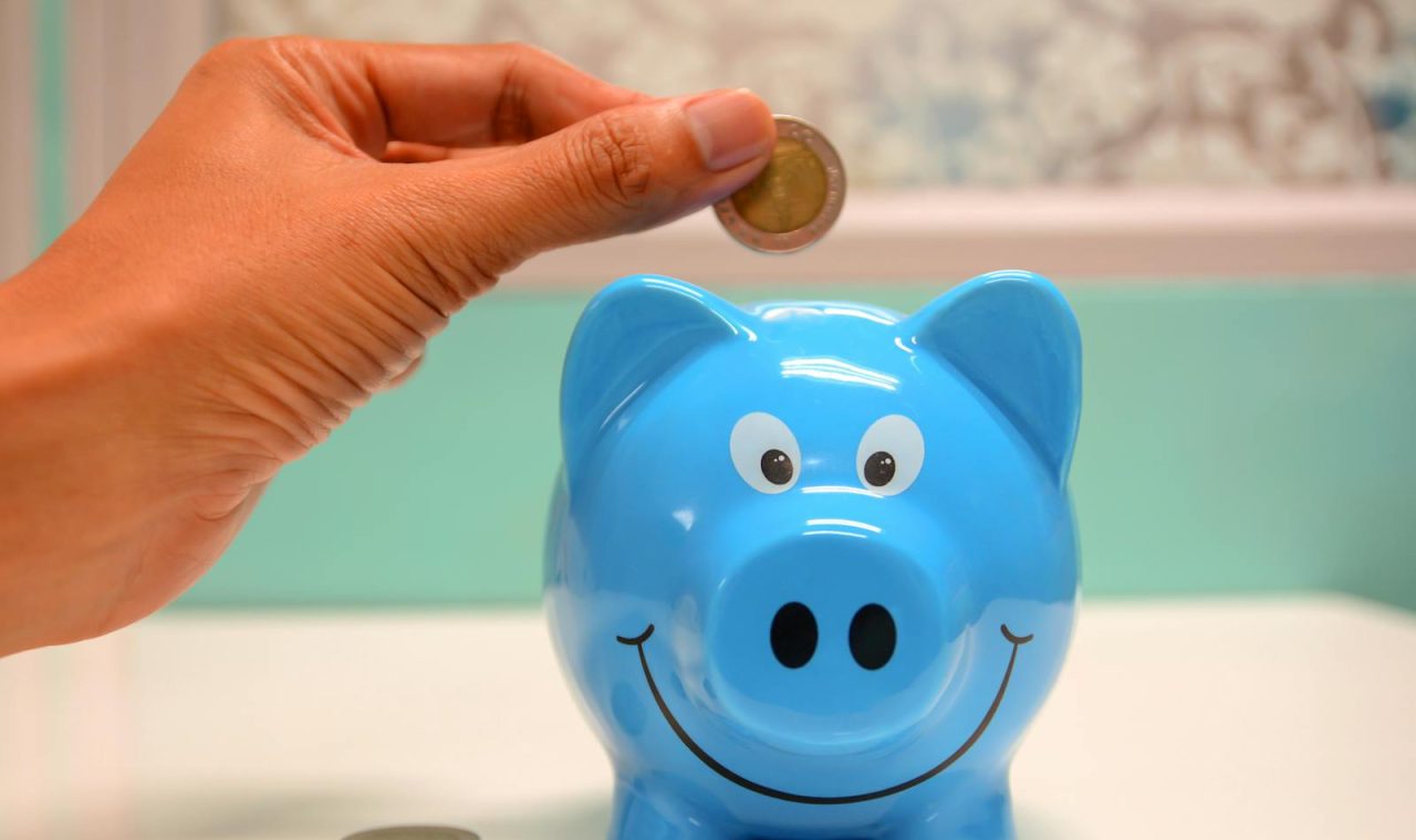 Hand inserting a coin into a blue piggy bank for savings and money management
