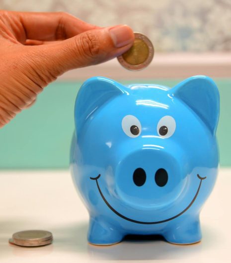 Hand inserting a coin into a blue piggy bank for savings and money management