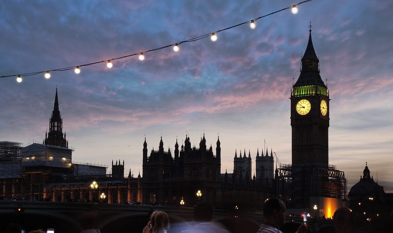 People stroll along the River Thames at dusk, with the iconic Big Ben illuminated in the background