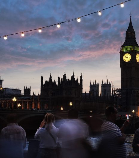 People stroll along the River Thames at dusk, with the iconic Big Ben illuminated in the background