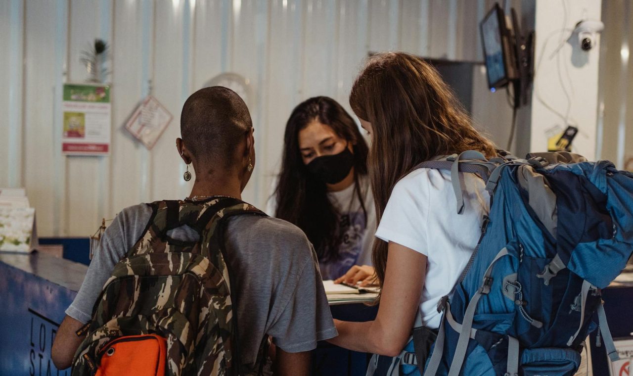 Two travelers with backpacks check in at a hostel reception counter