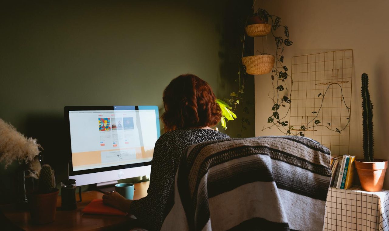 A woman sits at a home office desk with a desktop monitor, emphasising remote work and modern technology