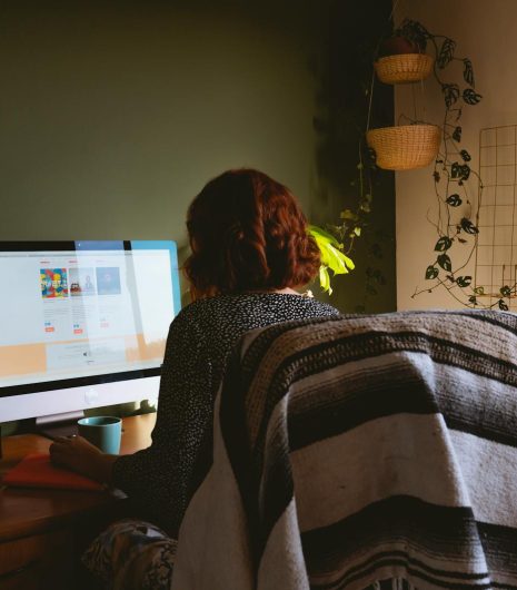 A woman sits at a home office desk with a desktop monitor, emphasising remote work and modern technology