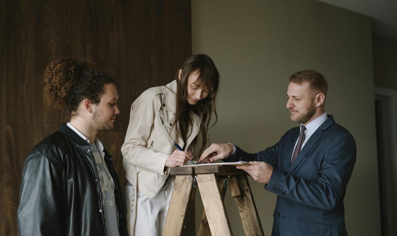 Three individuals signing a contract on a ladder inside a new house, symbolising a real estate deal