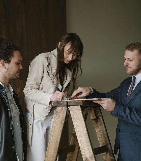 Three individuals signing a contract on a ladder inside a new house, symbolising a real estate deal