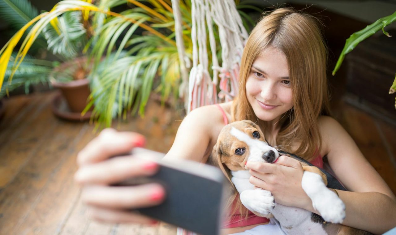 A smiling woman cuddles her cute beagle puppy while taking a selfie in a hammock
