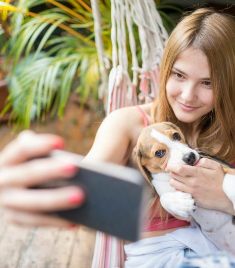 A smiling woman cuddles her cute beagle puppy while taking a selfie in a hammock