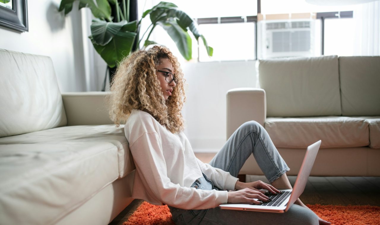woman sitting on floor and leaning on couch using laptop