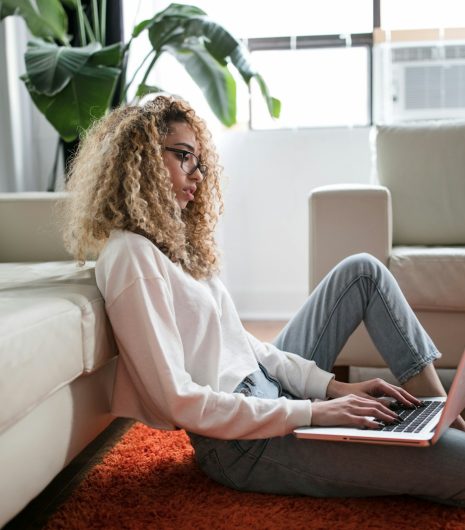 woman sitting on floor and leaning on couch using laptop