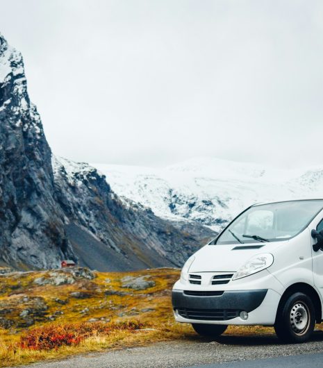 White delivery van parked on a scenic mountain road with snow-capped peaks in the background, autumn foliage nearby