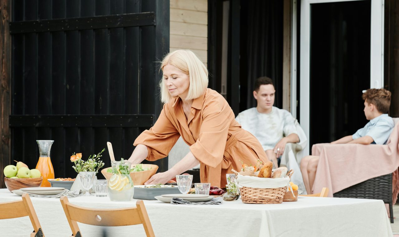 A woman prepares food at an outdoor table, surrounded by greenery and natural light