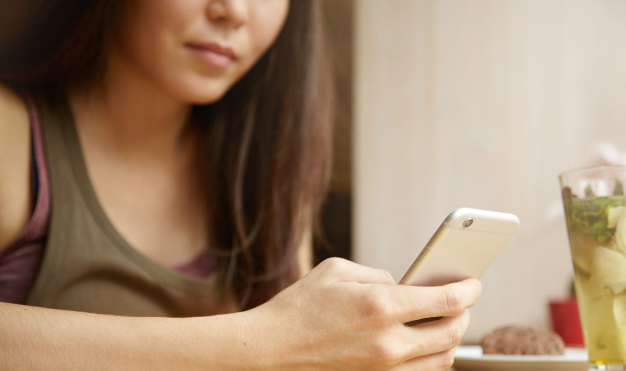 Close-up of a woman's hands using a mobile phone while sitting at a cafe table